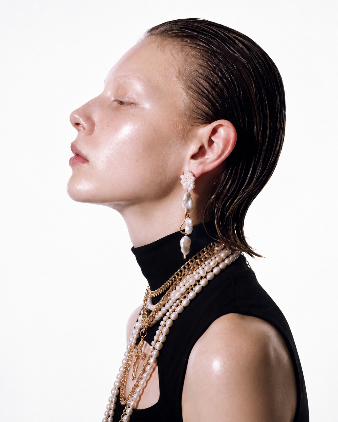 Model wearing layered gold necklaces, pearls, and pearl drop earrings